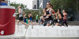 Marathon runners running, passing water station on urban street