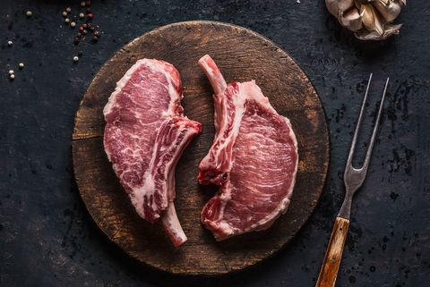 Marbled raw pork chops of Porco Iberico meat on round cutting board with meat knife. French Racks