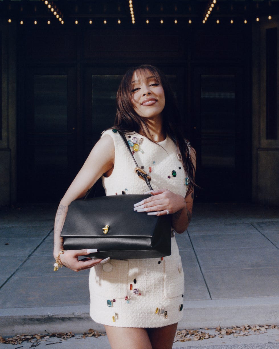 a person holding a black handbag while wearing a lightcolored dress with decorative elements