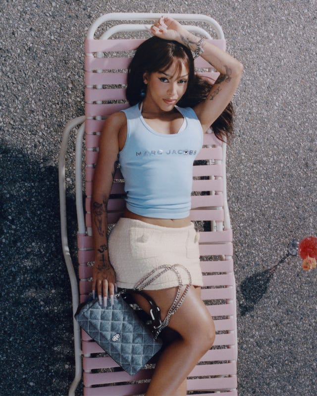 a person lounging on a pink lounge chair wearing stylish attire and holding a designer handbag