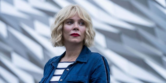 person wearing a striped shirt and denim jacket in front of a textured background