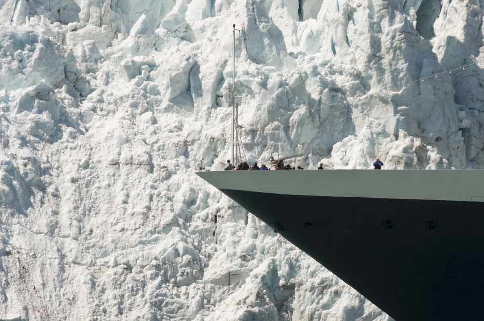 giant glacier dwarfing cruise ship as it goes by with people able to be seen on the top deck