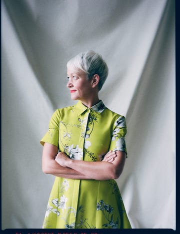 a person wearing a floralpatterned green dress stands with crossed arms against a neutral background