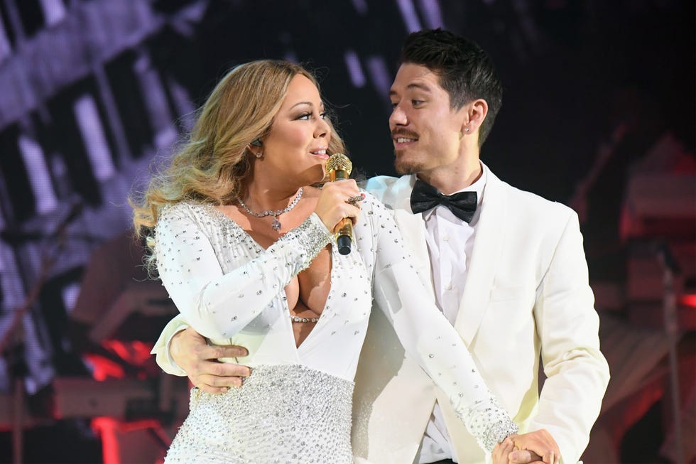 mariah carey dances with bryan tanaka as she sings into a wireless microphone she holds with one hand, they both were white formal attire