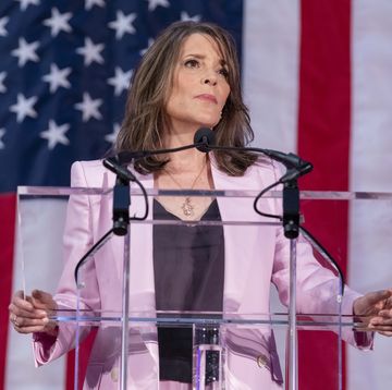 marianne williamson standing in front of an american flag and looking out over a podium