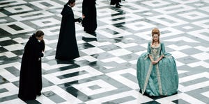 a publicity photo of emilia schule as marie antoinette, on a black and white tiled floor, with four men in black standing behind her