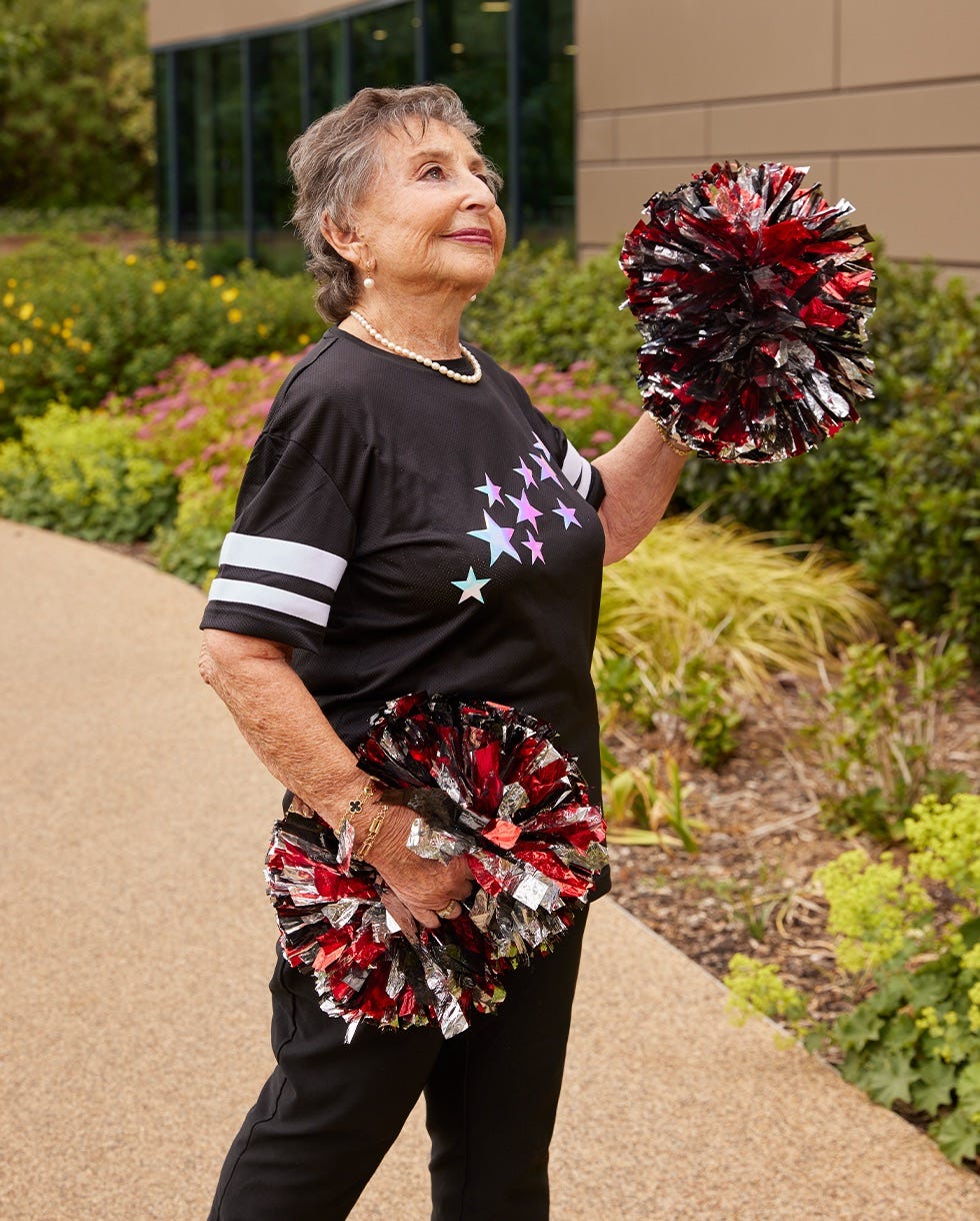an elderly woman cheerfully holding pompoms outdoors