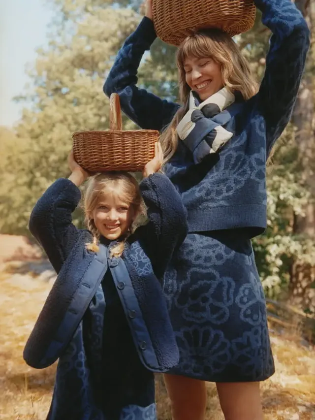 two individuals with woven baskets on their heads in a natural setting
