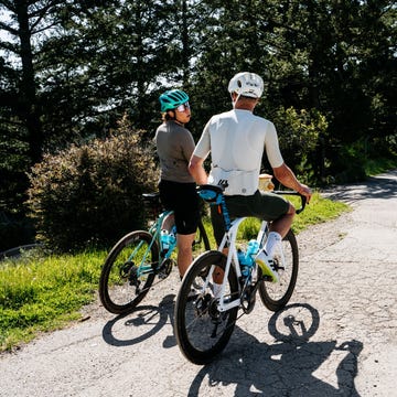 two cyclists pause on a winding road surrounded by nature two cyclists pause on a winding road surrounded by nature