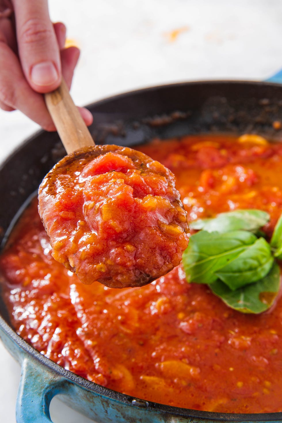 spoonful of marinara over a pot of marinara with basil leaves