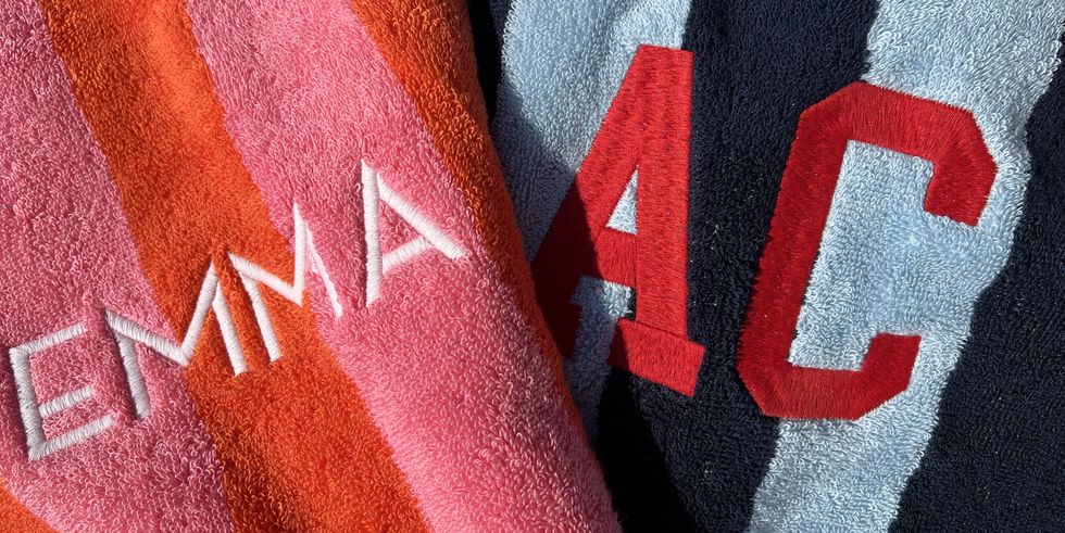 a close up of embroidery on two mark and graham cabana stripe beach towels that say emma and ac, good housekeeping's best beach towels