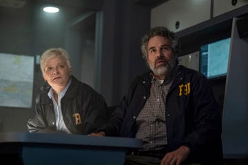 two individuals in fbi jackets seated at a table in a dimly lit room