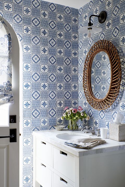 blue and white tile in a bathroom that has a round mirror over a marble top white vanity