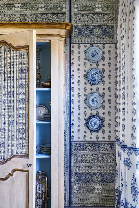 blue and white pattern covers the walls in a dining room and a cabinet hold dishes and serving pieces