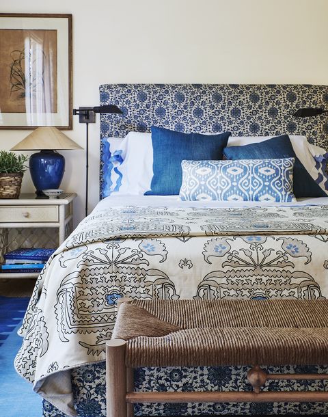 a blue and white pattern cloaks the headboard, bed skirt, and armchair cushions in a guest bedroom with a rush bench at the end