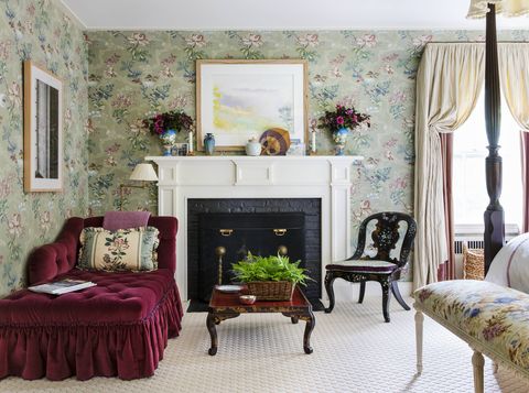 a plum velvet chaise sits snugly in the corner of a bedroom next to a fireplace