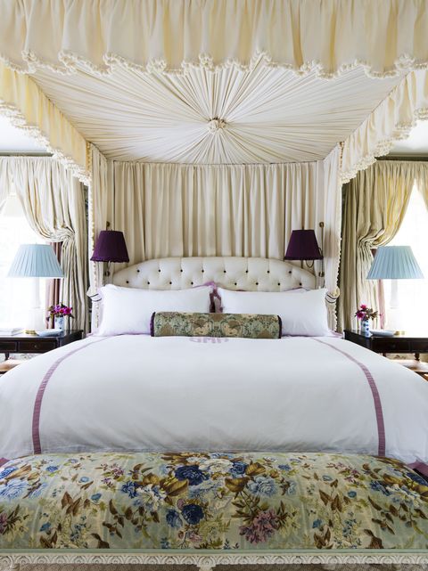 a grand caopy bed with white and lilac personalized bedding and a floral bench at the end