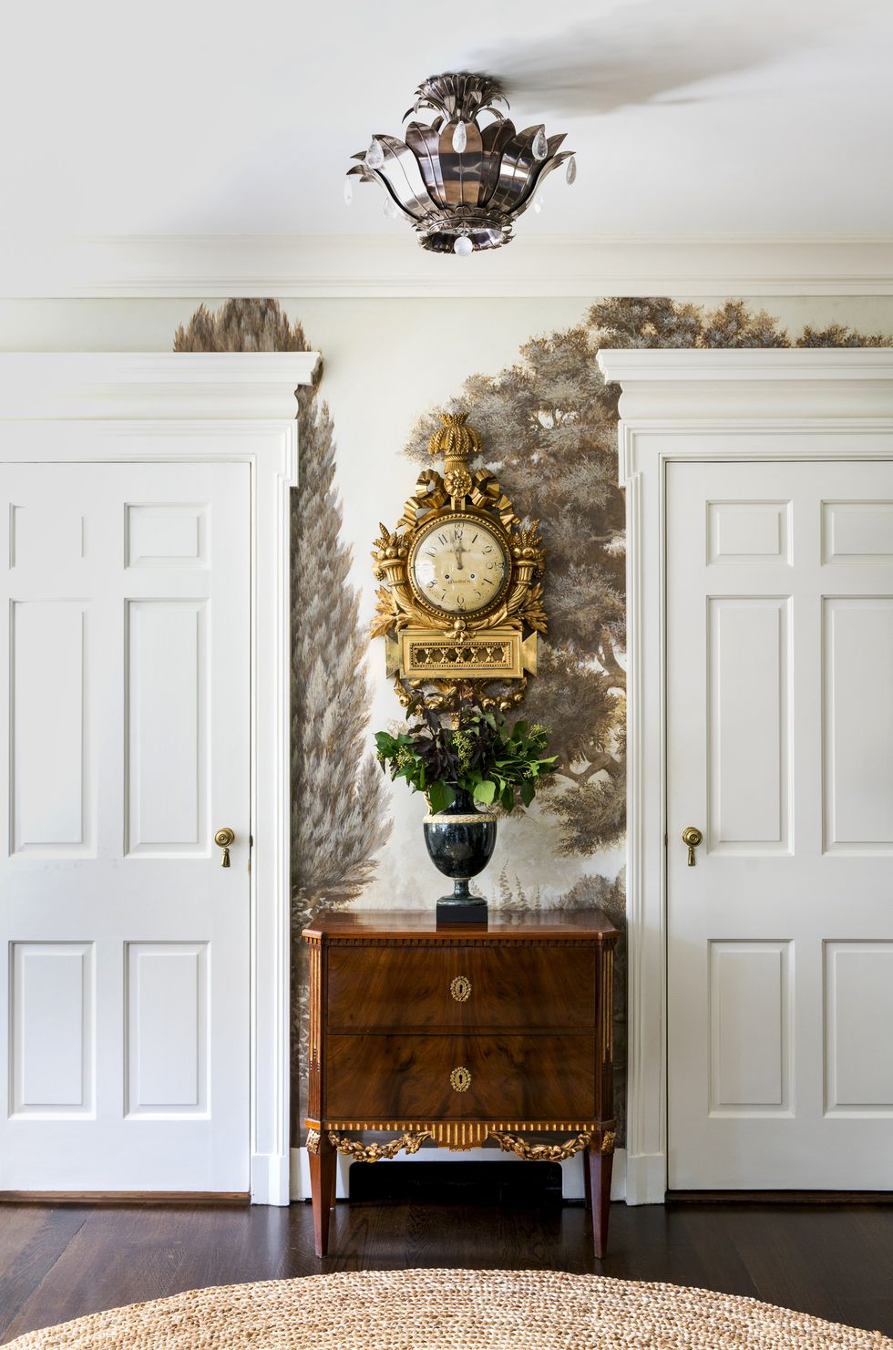 two tall white wood doors flank an antique chest and a clock from 1780 hangs above