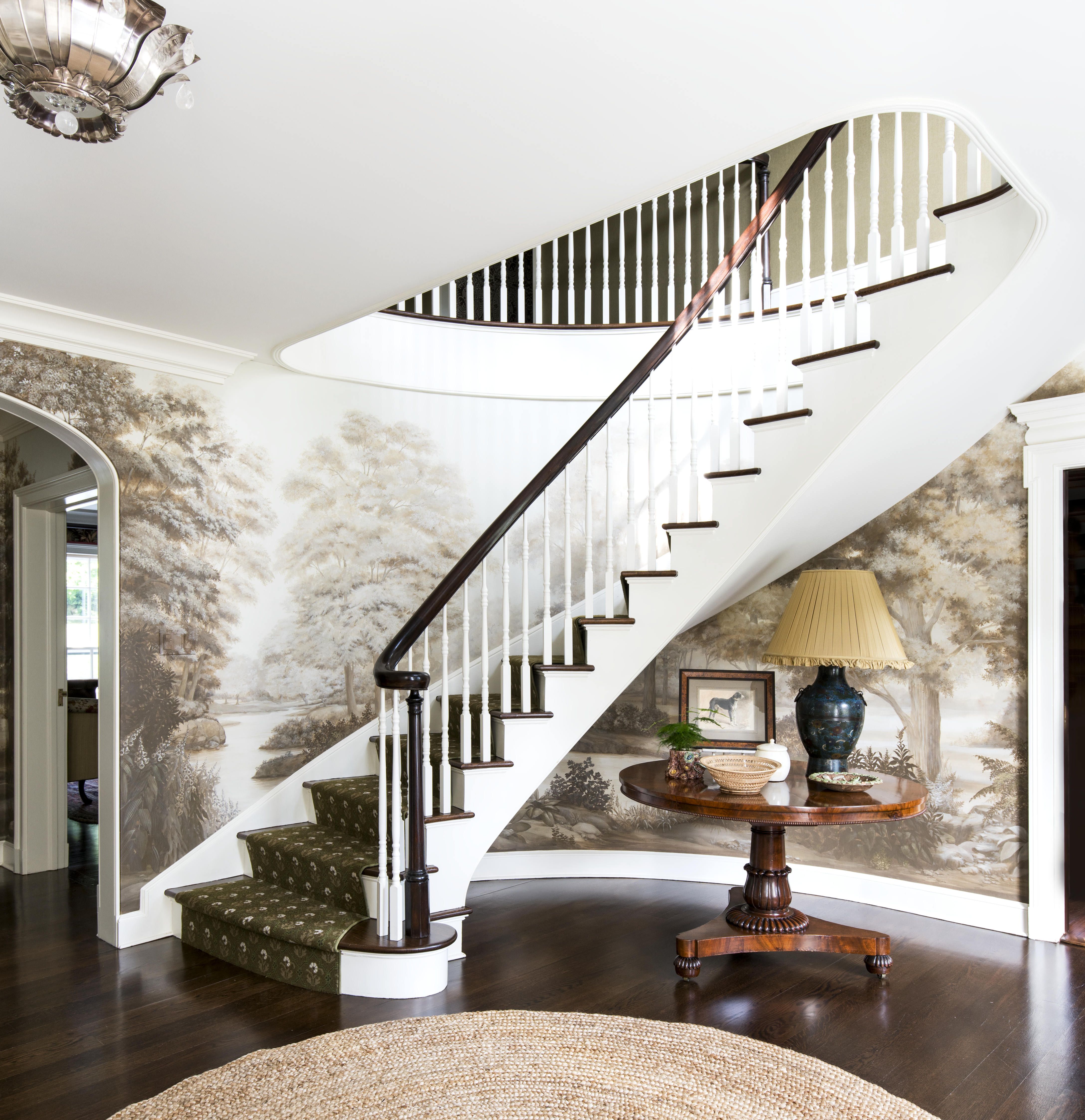a sweeping staircase in an entry with a sepia toned mural on the curved walls