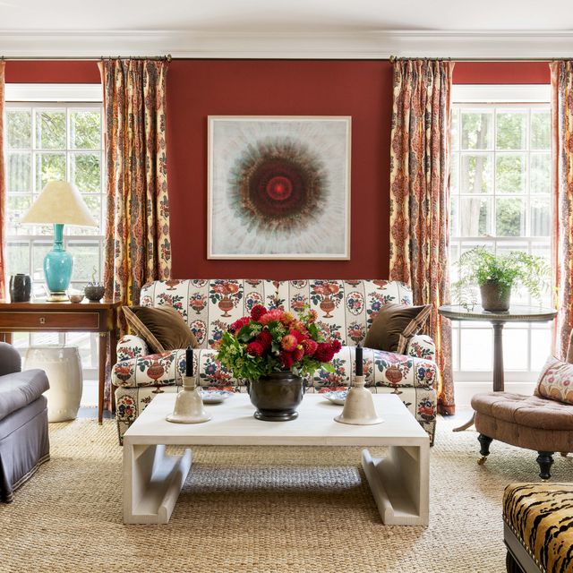 brick red walls with two windows that frame a patterned sofa with a coffee table and two chairs