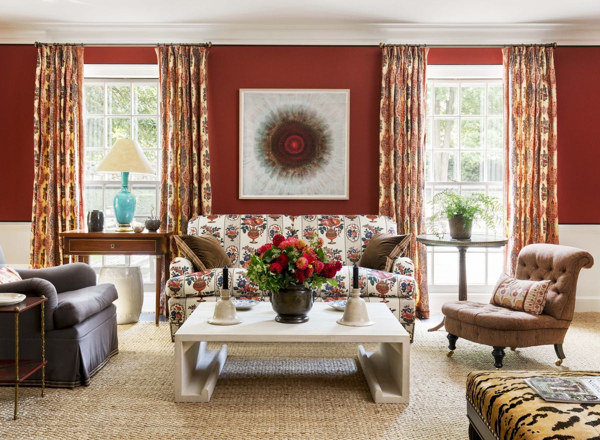 brick red walls with two windows that frame a patterned sofa with a coffee table and two chairs