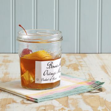 a marmalade jar with a drink in it, with a cherry and orange peel garnish