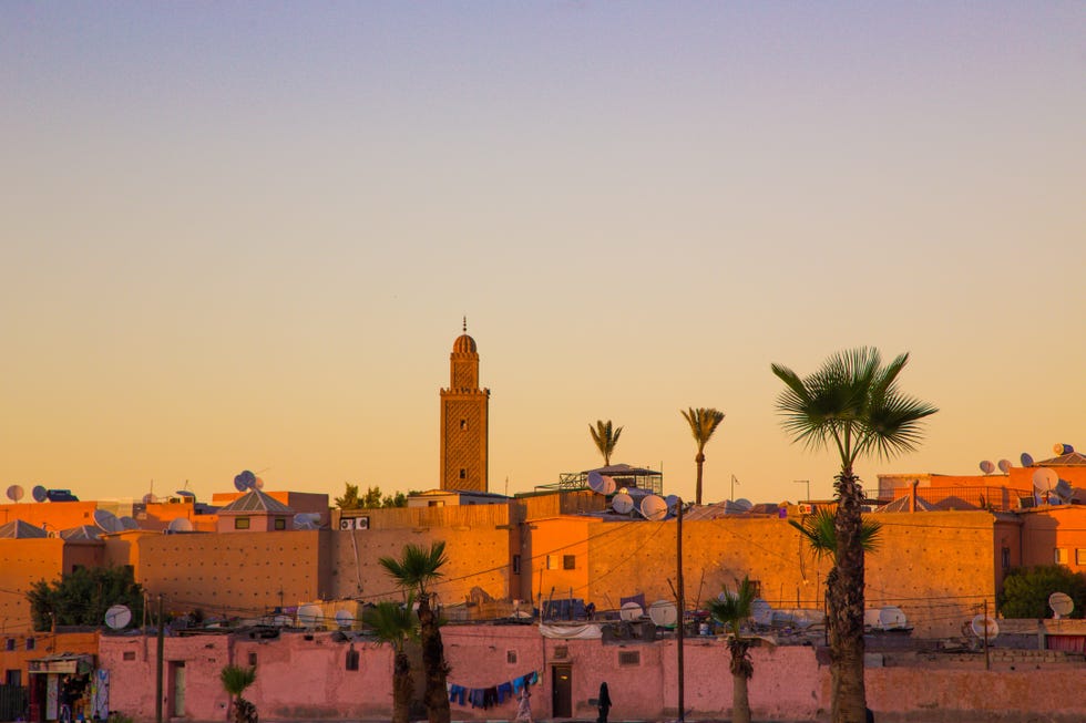 Fas'taki seyahat tatilleri sırasında gökyüzünde cami siluetleri ve güzel renkler bulunan bina terasından gün batımı sırasında Marakeş şehir manzarası.
