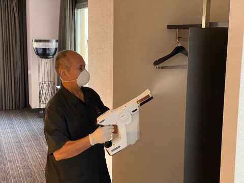 man in a hotel room using a sprayer to disinfect open closet