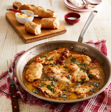 crispy chicken in a pan with a buttery sauce, and bread on a cutting board near by