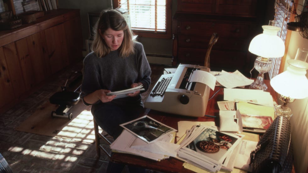 a person reviewing documents while seated at a cluttered desk with a typewriter and scattered papers