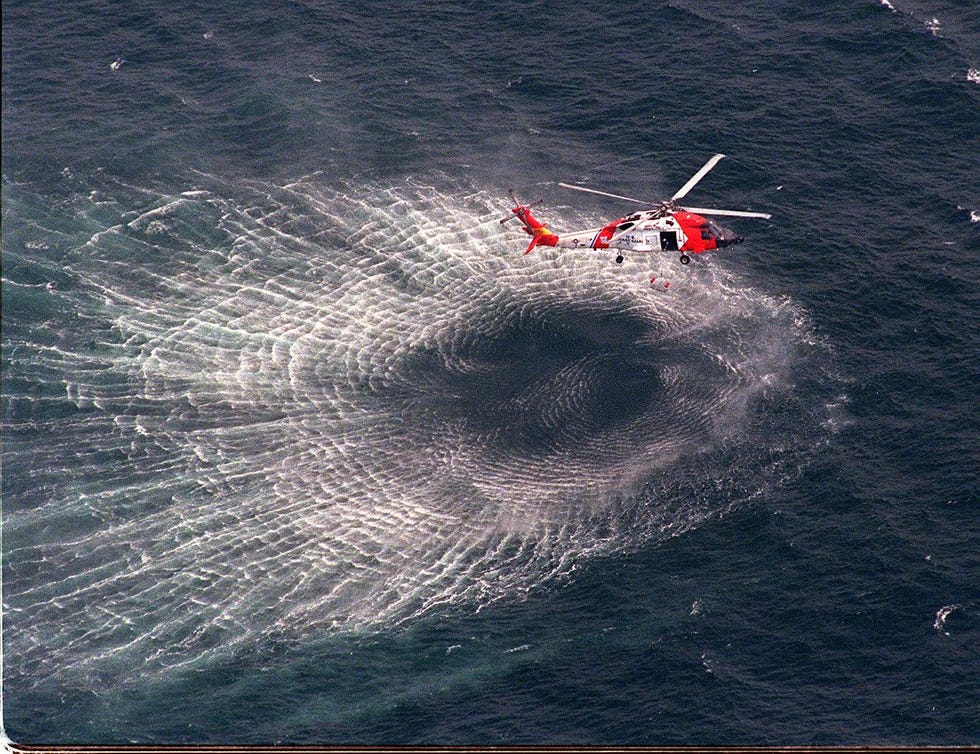 a coast guard helicopter hovers near the oceans surface, causing wake in the empty water