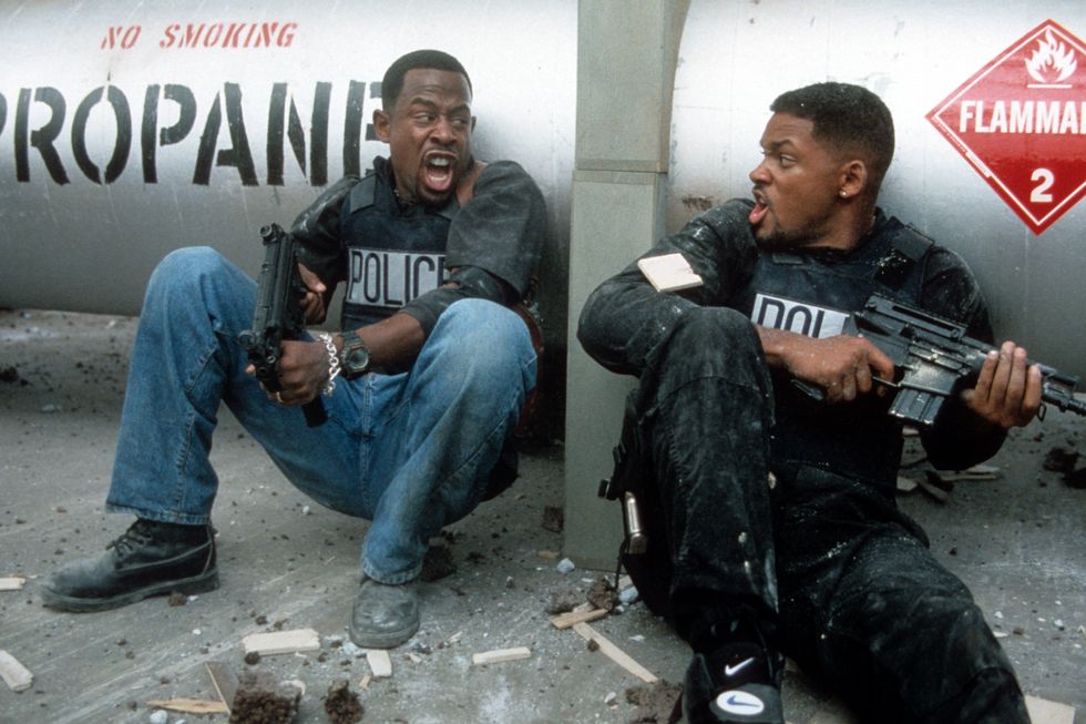 martin lawrence an will smith sit on the ground against a propane tank and yell at each other, each wears a police vest and holds a gun
