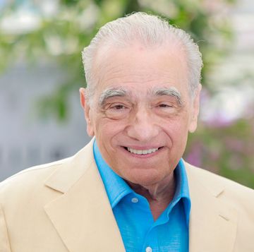 martin scorsese smiles at the camera, he wears a cream suit jacket with a bright blue collared shirt unbuttoned at the neck