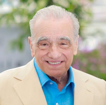 martin scorsese smiles at the camera, he wears a cream suit jacket with a bright blue collared shirt unbuttoned at the neck