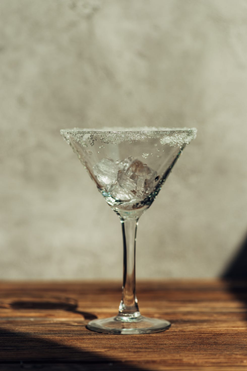 martini glass with ice decorated with sugar on wooden surface in sunlight