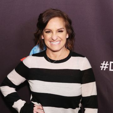 mary lou retton smiles and stands with one hand on her hip, she wears a black and cream colored shirt and small silver necklace