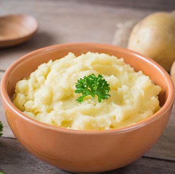 mashed potato in bowl and fresh potatoes on wooden table