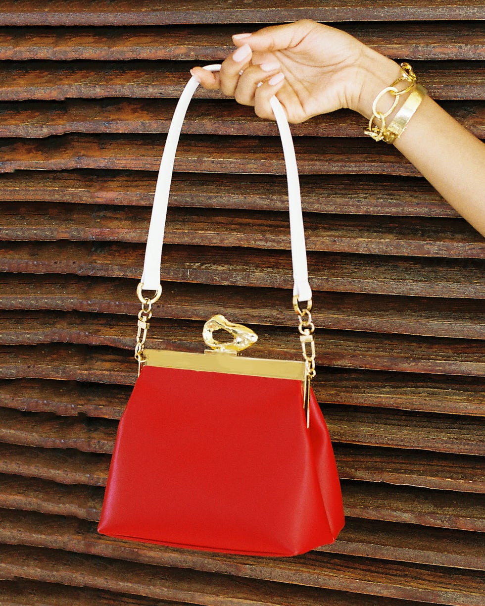 a red handbag held by a hand against a textured background