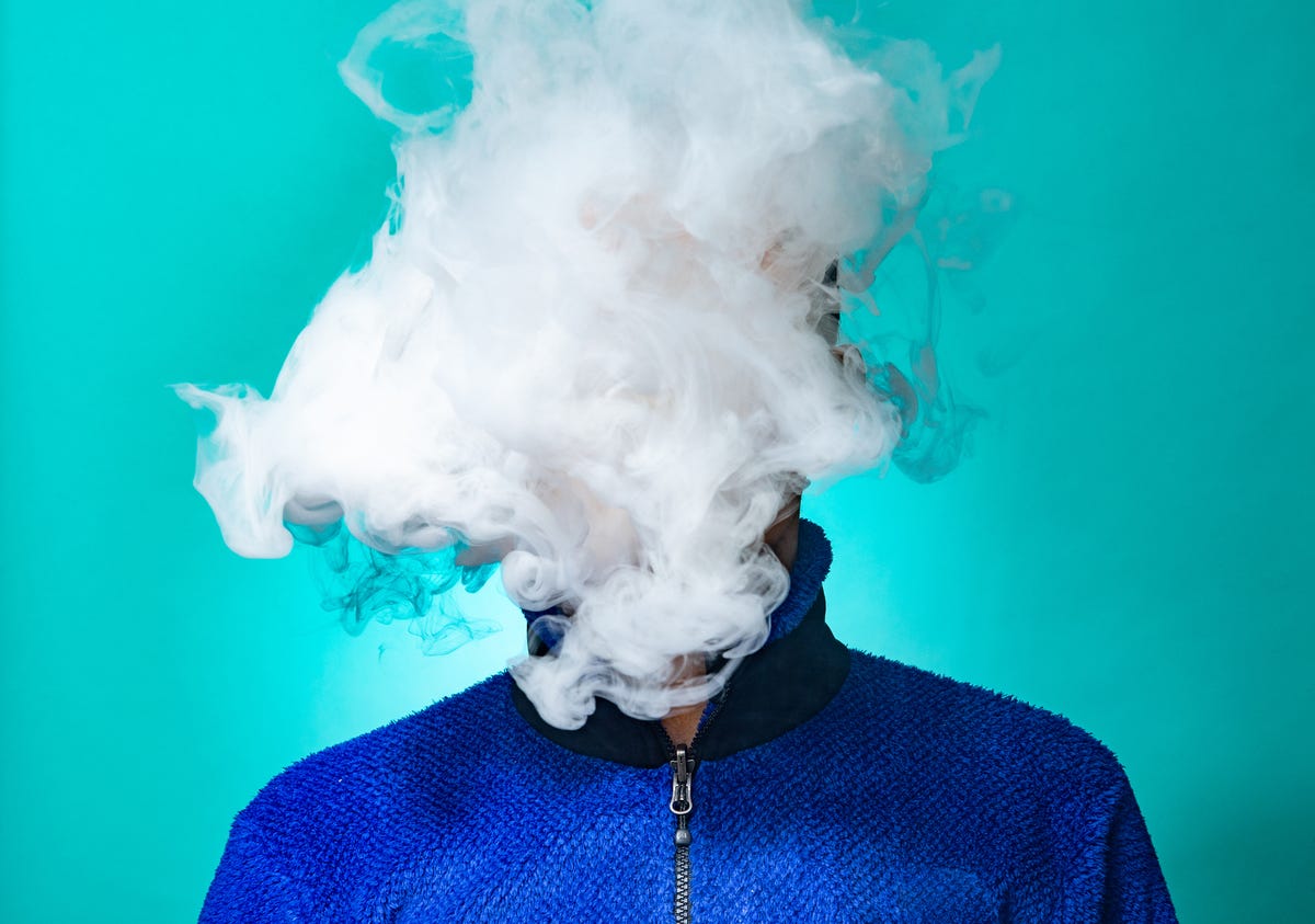 a masked man smoking vape and exhaling