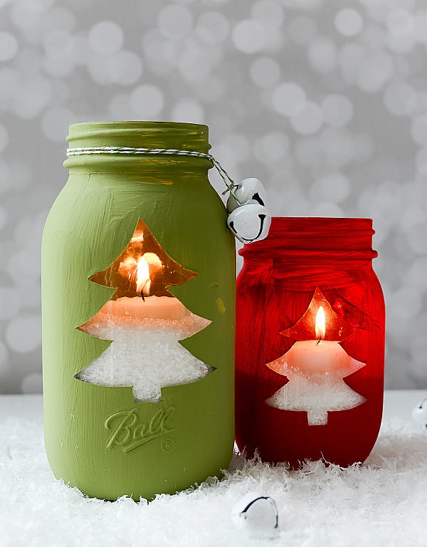 two mason jars, one red, one green, with christmas tree cutouts showing candlelight