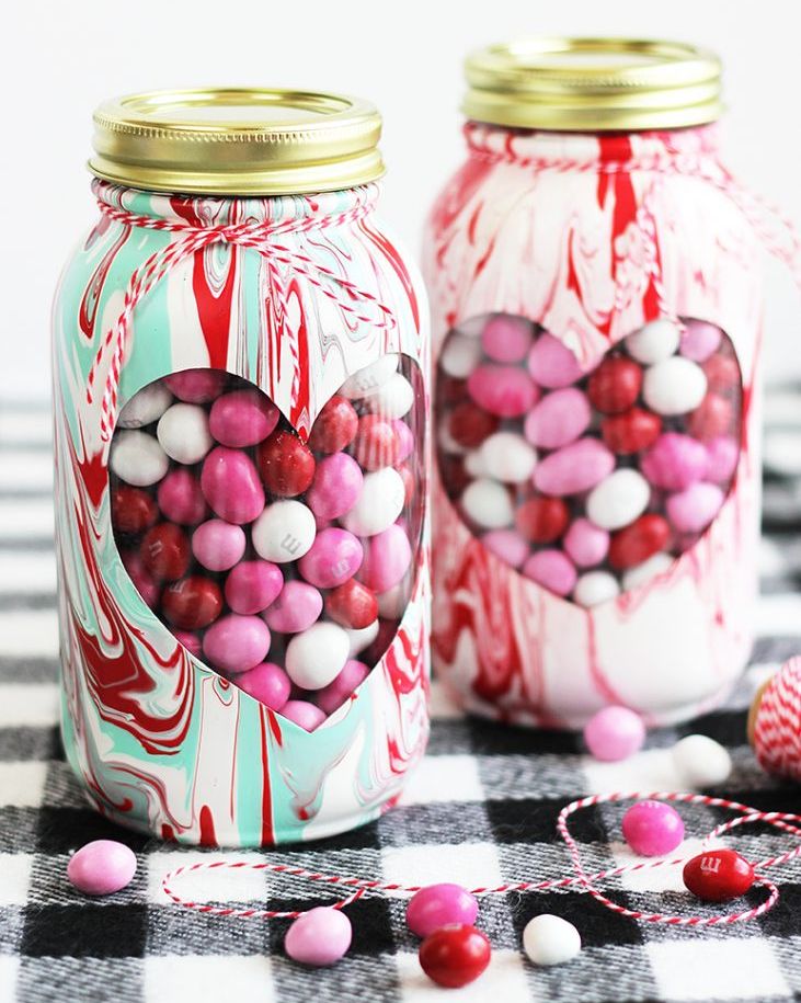 two mason jars patterned with acrylic paint with hearts cut out and red, white and pink mms showing through the cut out