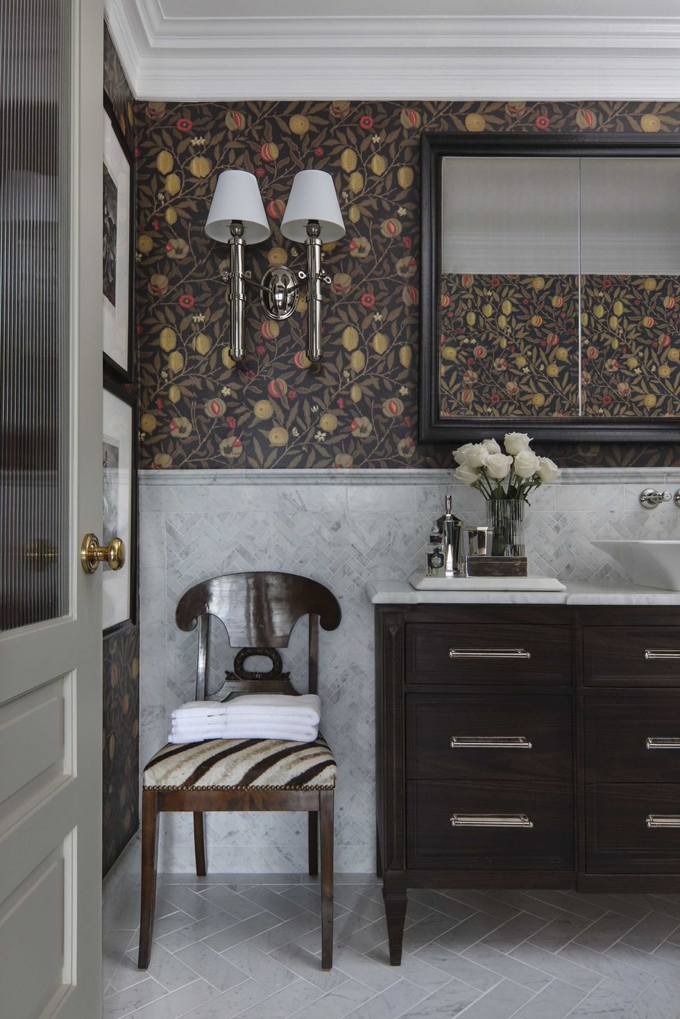 bathroom, wooden cabinets, marble tiling on floor and walls, floral wallpaper, sconces