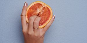 cropped studio shot of an unrecognizable woman putting her fingers into a grapefruit against gray background