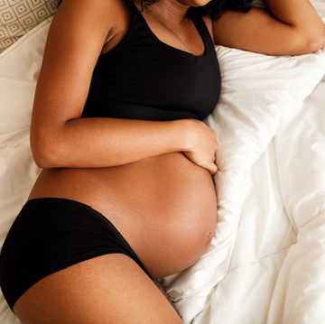 pregnant woman in black underwear and bra laying in bed