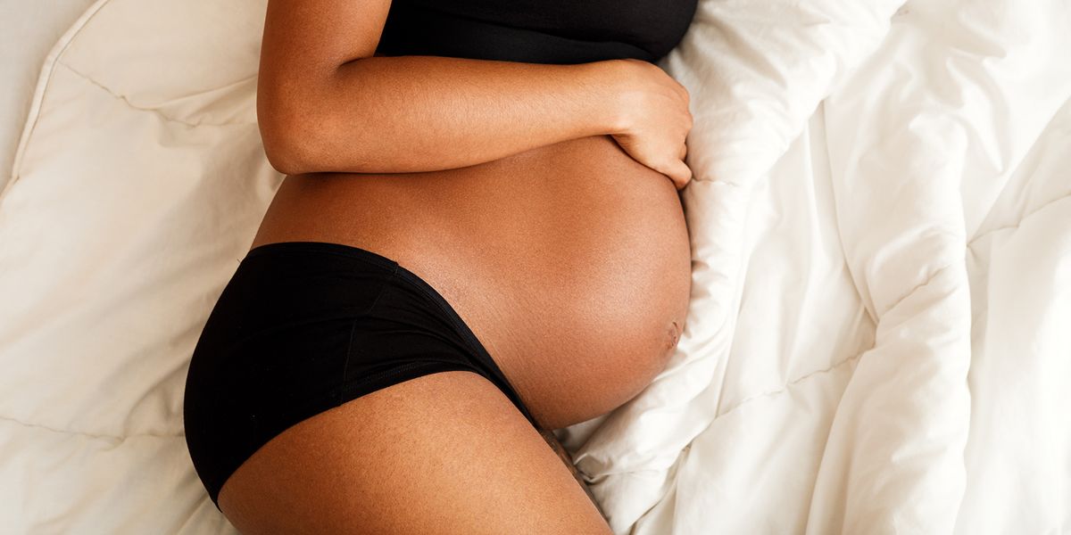 pregnant woman in black underwear and bra laying in bed