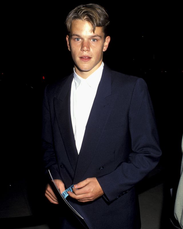 matt damon looks at the camera with a neutral expression on his face, he holds a booklet and wears a navy blue jacket and white collared shirt