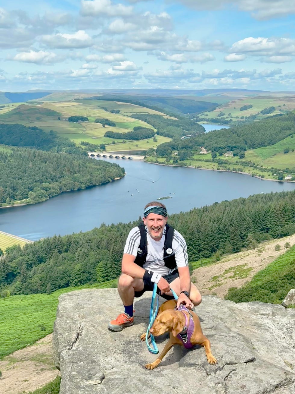 a man and a dog are perched on a rocky ledge overlooking a scenic landscape