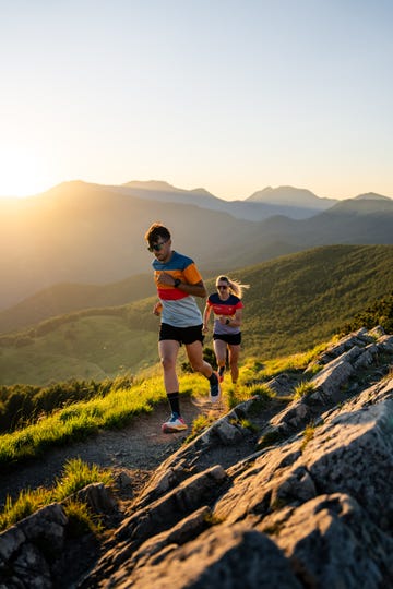 two individuals running along a mountain trail during sunset