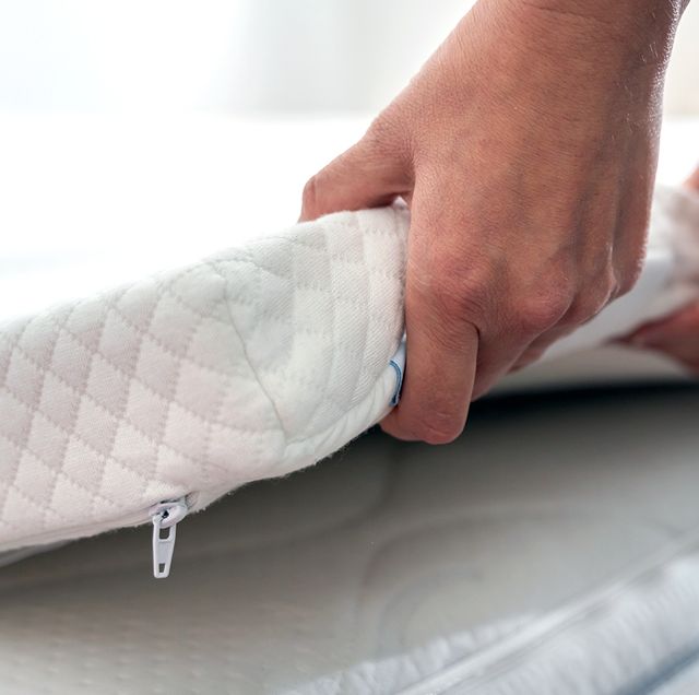 hands adjusting mattress topper on bed