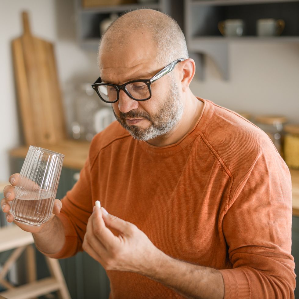 mature adult man in cozy interior of home kitchen taking medication